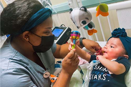 Staff playing with a smiling baby with a baby rattle