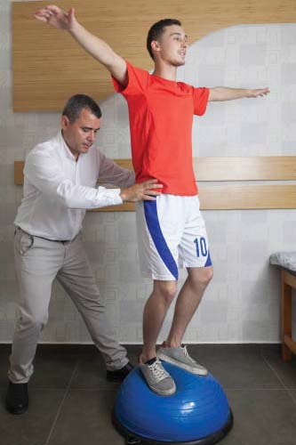 Teenage boy standing on balance ball with assistance